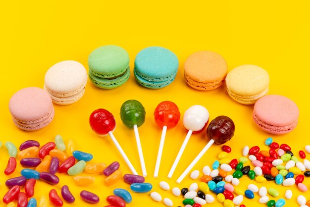 Macarons franceses com vista de cima, pirulitos e doces coloridos espalhados em confeitaria amarela e doce