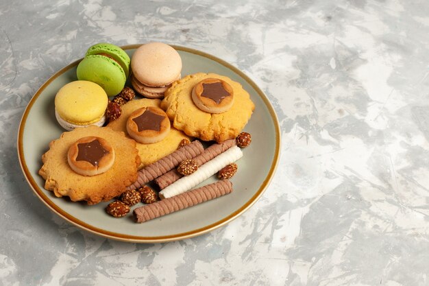 Macarons franceses de vista frontal com bolos e biscoitos na superfície branca