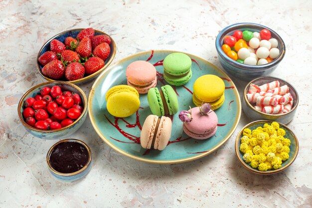 Macarons franceses de vista frontal com doces e frutas vermelhas em um bolo de biscoito de biscoito de mesa branca