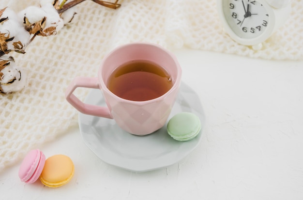 Macaroons coloridos com chá verde à base de plantas na xícara de cerâmica rosa e Pires na mesa