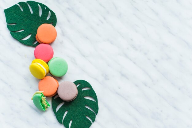 Macaroons coloridos com monstera falso deixa sobre fundo de mármore branco