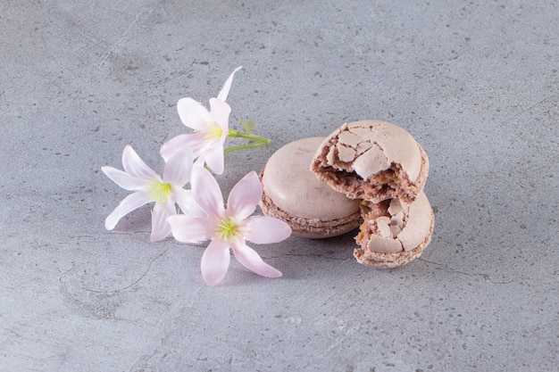 Macaroons marrons cremosos com flores pastel na mesa de mármore.