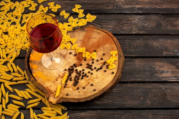 Macarrão amarelo cru, juntamente com pimenta e garrafa de vinho em uma mesa redonda de madeira sobre uma mesa marrom