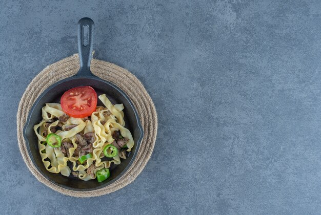 Macarrão com pedaços de carne na frigideira preta.