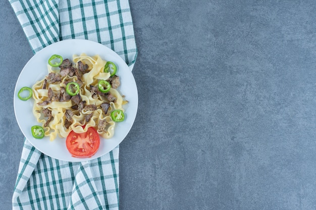 Macarrão cozido com pedaços de carne na chapa branca.