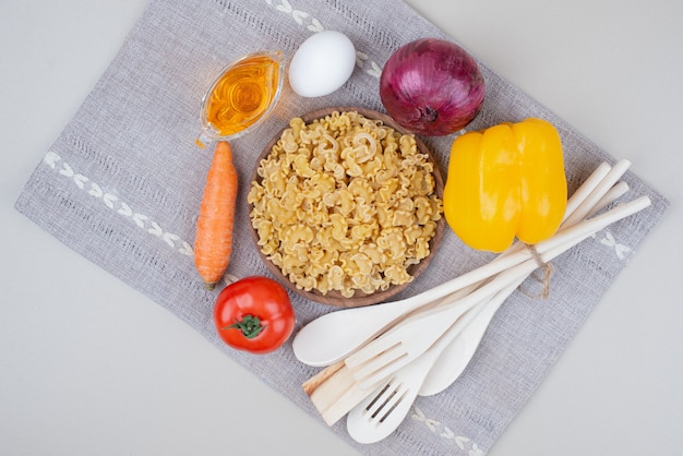 Macarrão cru com legumes em um prato de madeira na toalha de mesa