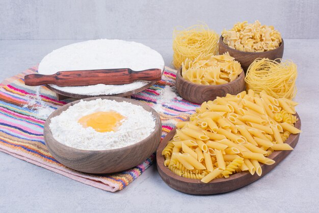 Macarrão cru em tigelas de madeira com gema e farinha