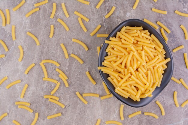 Macarrão cru em uma tigela de cerâmica preta no mármore.