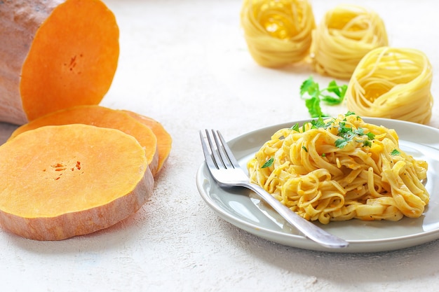 Macarrão de abóbora alfredo fettucine em uma placa de cerâmica com fatias de abóbora crua fresca. Outono refeição para o almoço. Receita de abóbora.