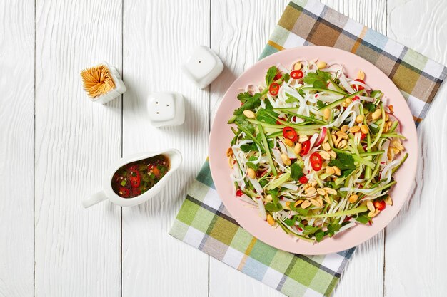 Macarrão de arroz e salada de legumes em um prato sobre uma mesa de madeira com molho em uma molheira, cozinha asiática, visão horizontal de cima, plana leigos