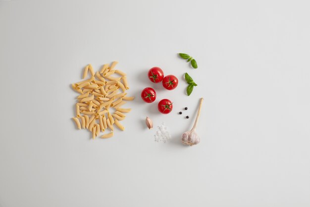 Macarrão de ovo cru penne com tomate cereja de ingredientes orgânicos frescos, alho, manjericão, sal marinho, pimenta em grão. Conceito de alimentação e nutrição saudável. Produtos para cozinhar a cozinha tradicional italiana.