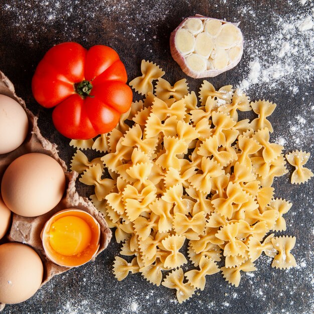 Macarrão de vista superior com ovos, tomate e alho no fundo texturizado escuro.