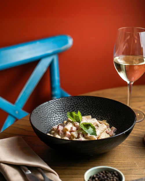 Macarrão em chapa preta um copo de vinho branco na mesa de madeira com fundo de cadeira azul