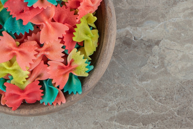 Foto grátis macarrão farfalle colorido em uma tigela de madeira.