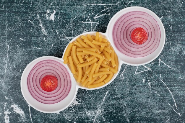 Macarrão fresco despreparado com fatias de cebola e tomate cereja.