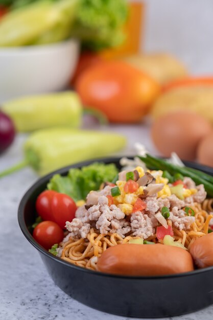 Macarrão frito com carne de porco picada, edamame, tomate e cogumelos em uma panela.