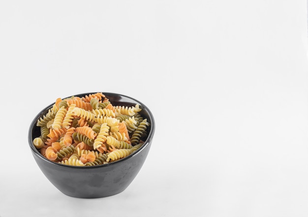 Macarrão fusilli colorido cru em tigela escura. Foto de alta qualidade