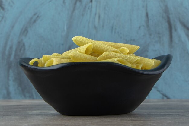 Macarrão penne cru em tigela preta.