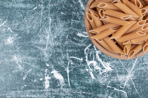 Macarrão penne cru marrom em uma tigela de madeira. Foto de alta qualidade