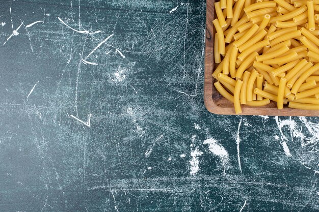 Macarrão penne cru na placa de madeira.