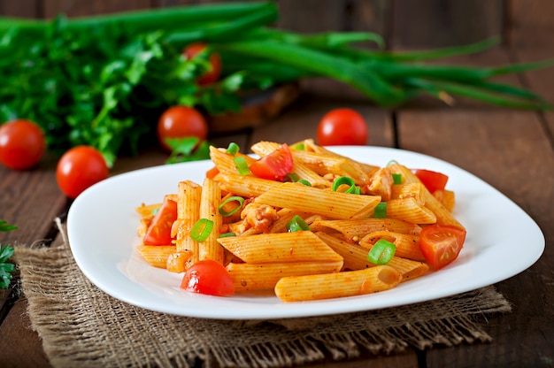 Foto grátis macarrão penne em molho de tomate com frango e tomate em uma mesa de madeira