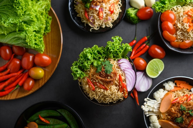 Macarrão picante na tigela com ingredientes na superfície de cimento preto, vista superior.