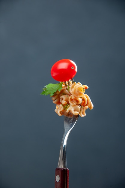 Macarrão rotini de vista frontal com tomate cereja no garfo em espaço livre de superfície cinza isolada