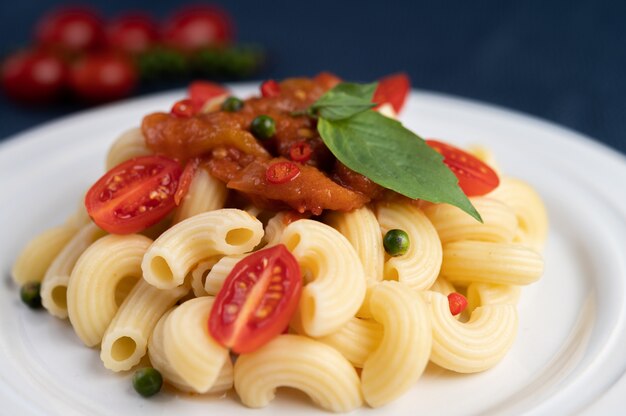 Macarrão salteado com tomate, pimentão, sementes de pimenta e manjericão em um prato branco.