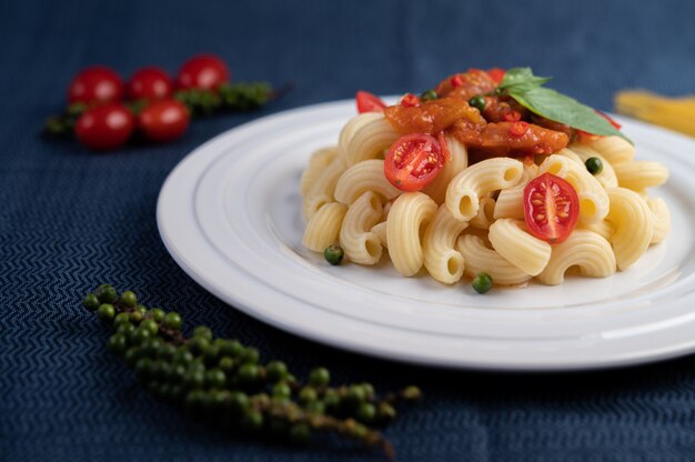 Macarrão salteado com tomate, pimentão, sementes de pimenta e manjericão em um prato branco.