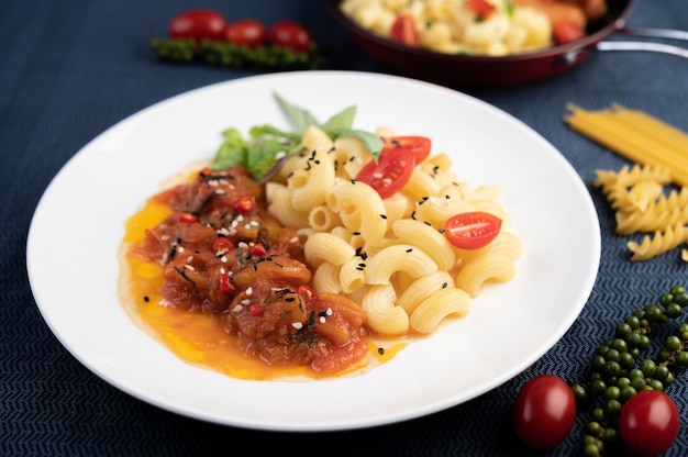 Macarrão salteado com tomate, pimentão, sementes de pimenta e manjericão em um prato branco.