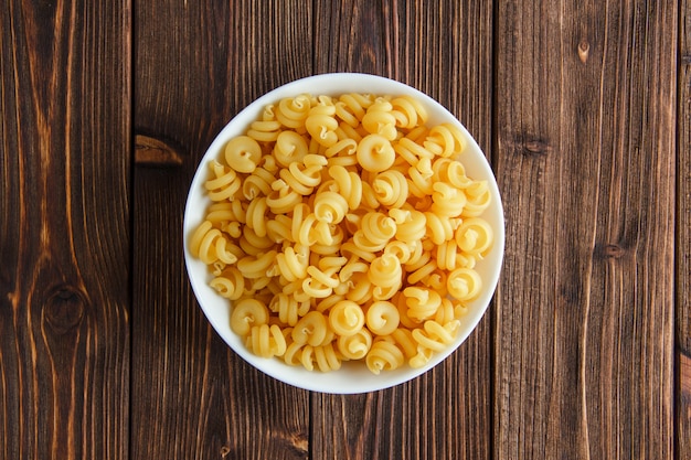 Macarrão seco em uma tigela sobre uma mesa de madeira. configuração plana.