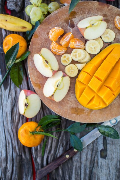 Maçãs tangerinas bananas mangas e uvas em uma placa de madeira