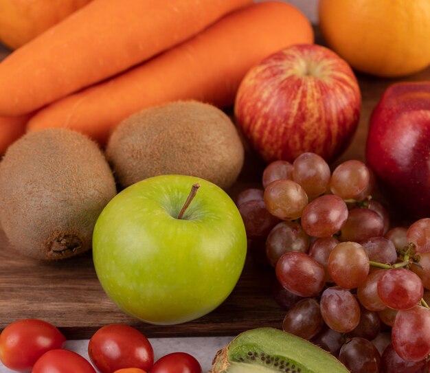 Maçãs, uvas, cenouras e laranjas colocadas juntas no chão.