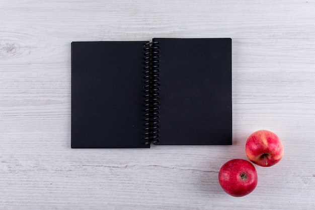 Foto grátis maçãs vermelhas de vista superior com espaço de cópia no caderno preto na horizontal de madeira branca