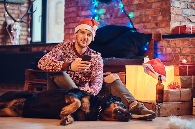 Macho atraente hipster barbudo com seu cachorro Rottweiler em uma sala com decoração de Natal.