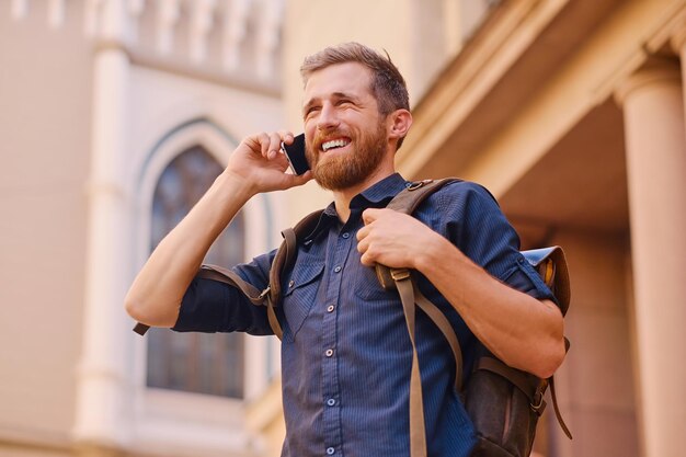 Macho barbudo com mochila falando por telefone inteligente em uma antiga cidade europeia.