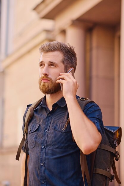 Macho barbudo com mochila falando por telefone inteligente em uma antiga cidade europeia.