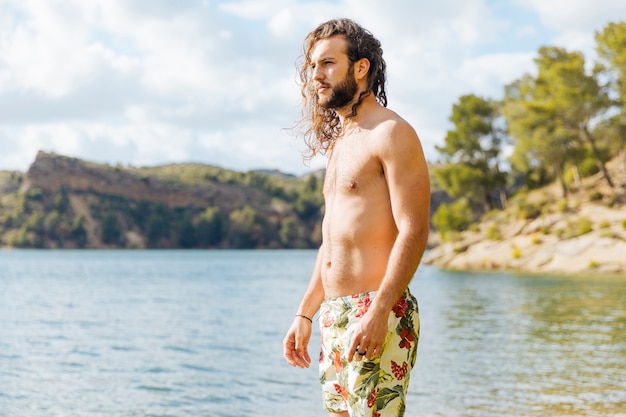 Macho barbudo jovem em pé perto do lago