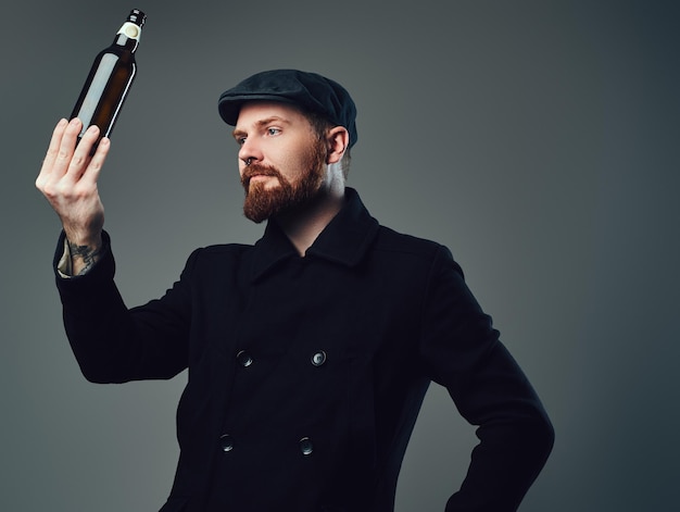 Foto grátis macho barbudo vestido com um boné de tweed preto e jaqueta de lã segura garrafa de cerveja.