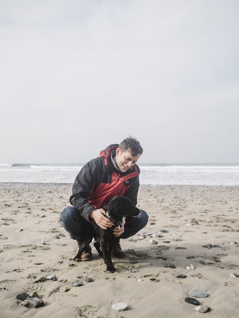 Macho brincando com um cachorro spaniel preto fofo na praia durante o dia