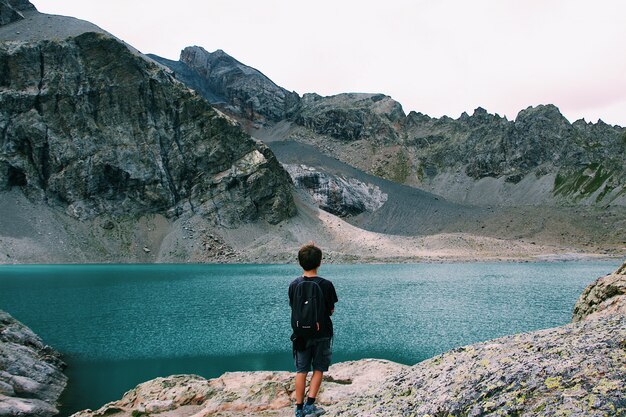 Macho com uma mochila em pé em um penhasco, apreciando a vista do mar perto de uma montanha