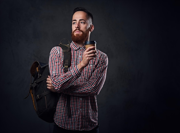 Macho de hipster barbudo ruivo em uma camisa de lã vermelha detém smartphone sobre fundo cinza.