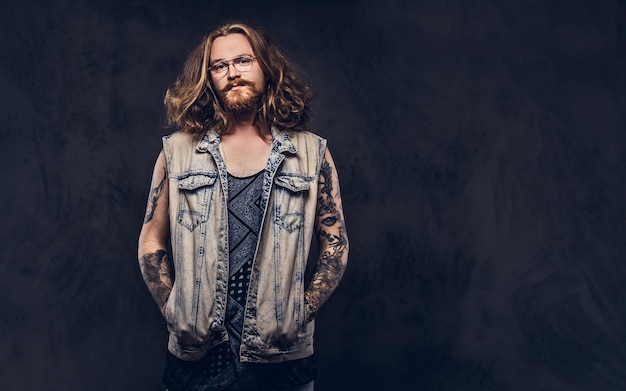 Foto grátis macho de hipster ruiva com cabelo longo luxuriante e barba cheia, vestido com roupas casuais, posando com as mãos nos bolsos em um estúdio, olhando para uma câmera. isolado no fundo escuro.