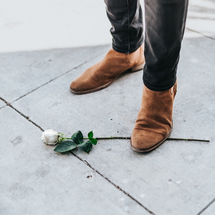 Foto grátis macho em botas de cowboy em pé em um único ramo de rosa branca