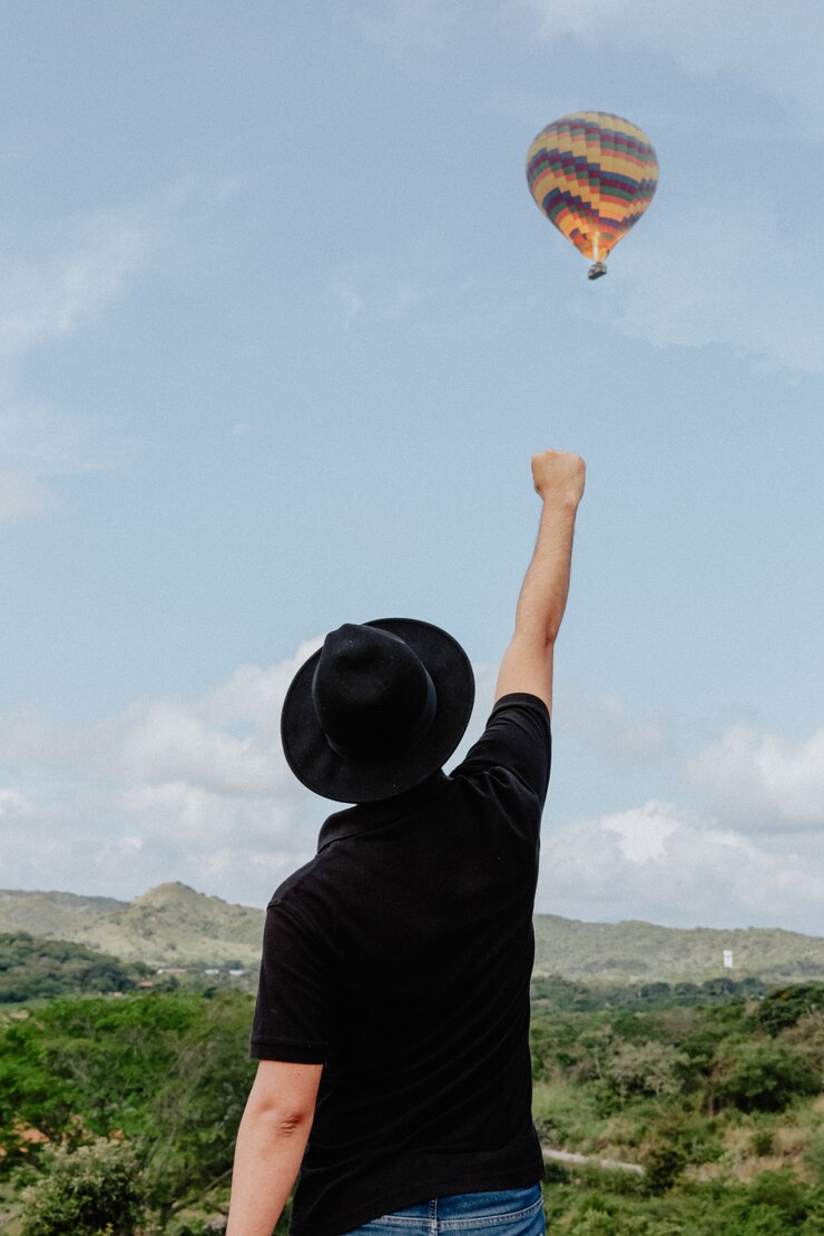 Foto grátis macho em pé com o braço e o punho levantado no ar e um balão de ar quente voando no fundo
