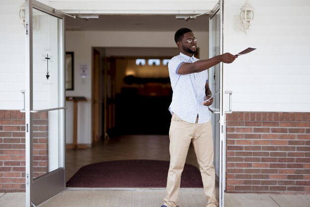 Macho em pé perto da igreja e distribuindo panfletos enquanto sorrindo