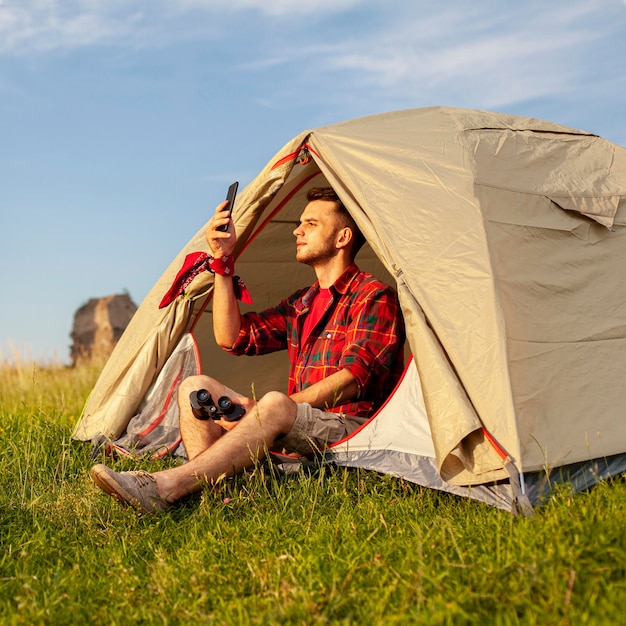 Macho na barraca de acampamento ao pôr do sol, a tirar uma selfie