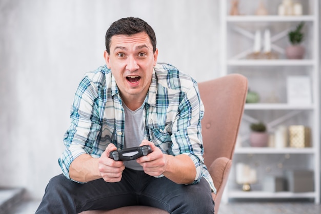 Foto grátis macho novo excitado que senta-se na poltrona e que joga com gamepad