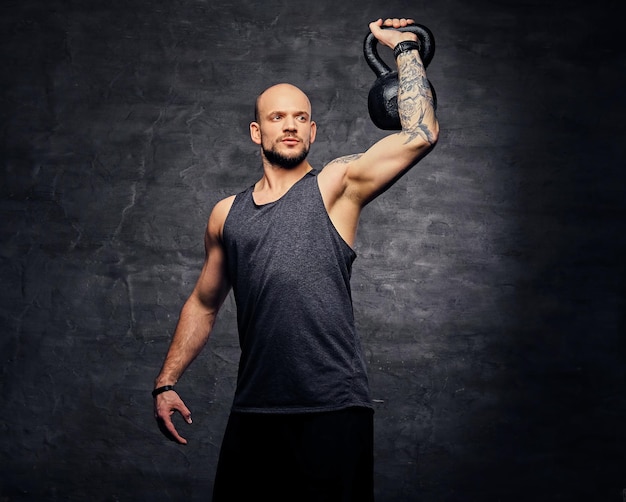 Foto grátis macho tatuado de cabeça raspada atlético fazendo treino de ombro com o kettlebell.