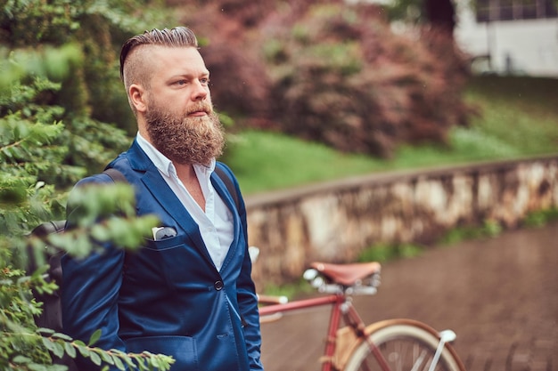 Foto grátis macho vestido com roupas casuais, de pé com uma bicicleta retrô em um parque da cidade.